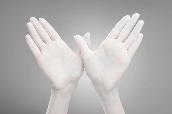 Cropped view of female hands painted in white showing bird-shape sign on grey — Stock Photo