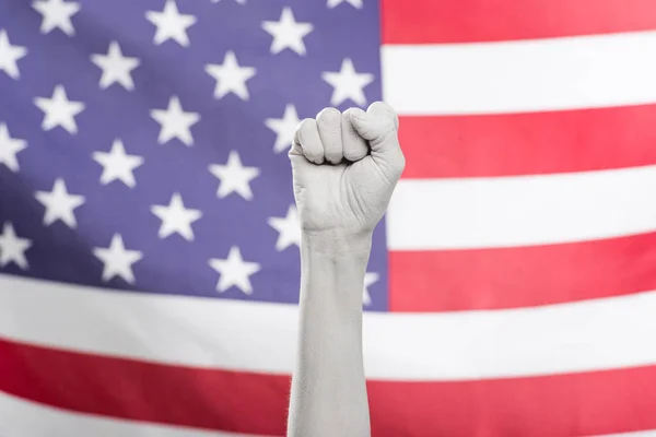 Обрезанный вид женской руки, выкрашенной в белый цвет, показывающий кулак возле американского флага — стоковое фото