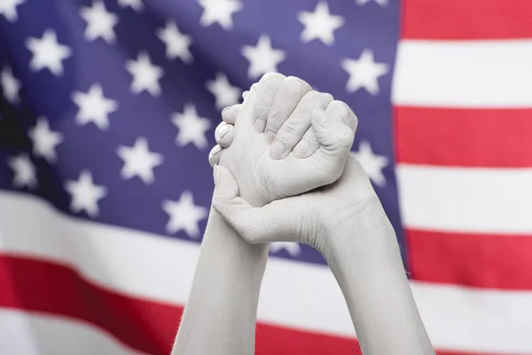 Vista recortada de las manos cerradas femeninas pintadas de blanco cerca de la bandera americana - foto de stock