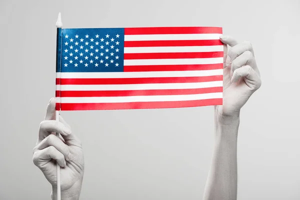 Cropped view of female hands painted in white holding american flag isolated on grey — Stock Photo