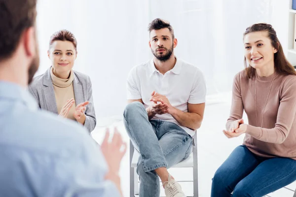 Enfoque selectivo de las personas aplaudiendo mientras miran al hombre durante la sesión de terapia de grupo - foto de stock