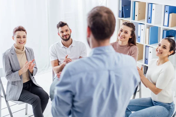 Smiling people applauding while looking at man during group therapy session — Stock Photo