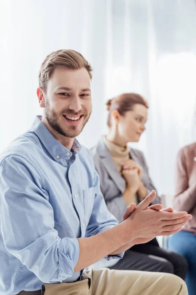 Selective focus of smiling man looking at camera and applauding during group therapy session — Stock Photo