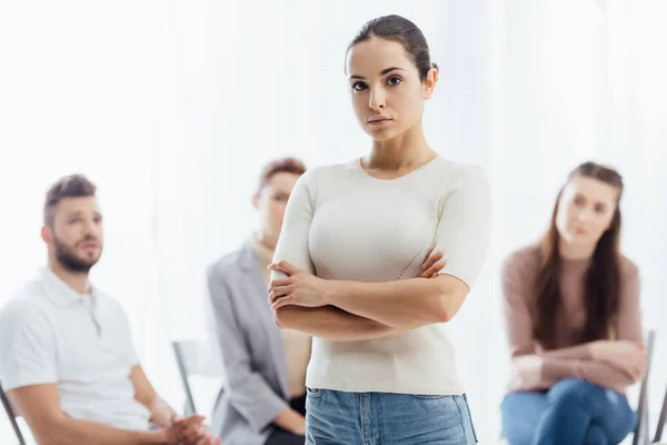 Woman with arms crossed looking at camera while people sitting during group therapy session — Stock Photo