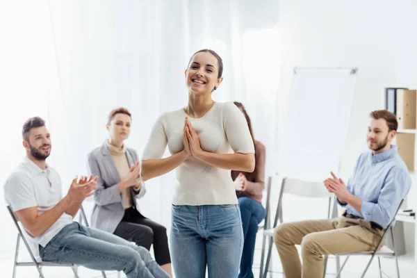 Lächelnde Frau, die in die Kamera schaut, während Menschen während einer Gruppentherapie auf Stühlen sitzen — Stockfoto