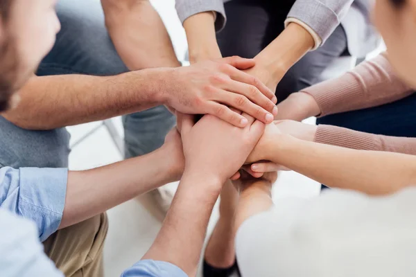 Vista recortada de personas que se apilan las manos durante la sesión de terapia de grupo - foto de stock