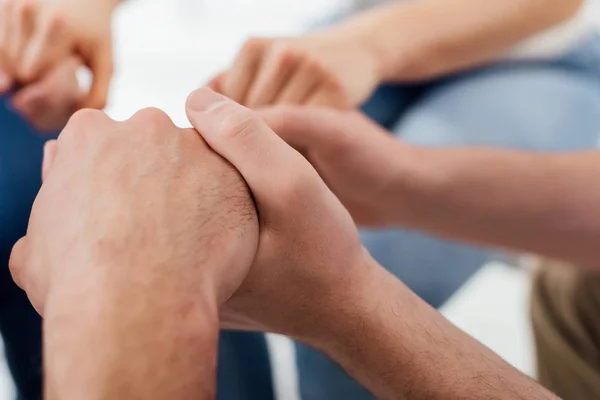 Обрезанный вид мужчин, держащихся за руки во время групповой терапии — стоковое фото