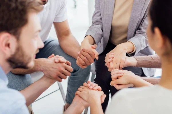 Vista recortada de personas cogidas de la mano durante la sesión de terapia de grupo - foto de stock