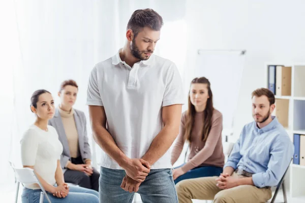 Selective focus of man looking away while people sitting during group therapy session — Stock Photo