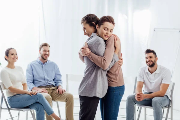 Women hugging while group of people sitting and smiling during therapy session — Stock Photo