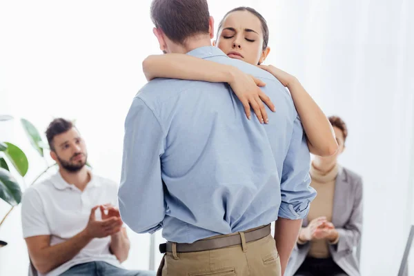 Enfoque selectivo de la mujer abrazando al hombre durante la sesión de terapia de grupo - foto de stock