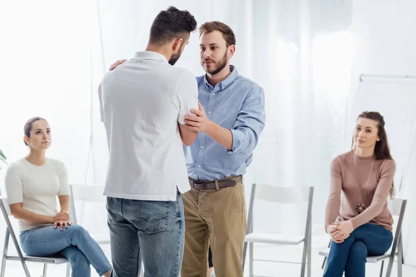 Man cheering another man while people sitting on chairs during group therapy session — Stock Photo