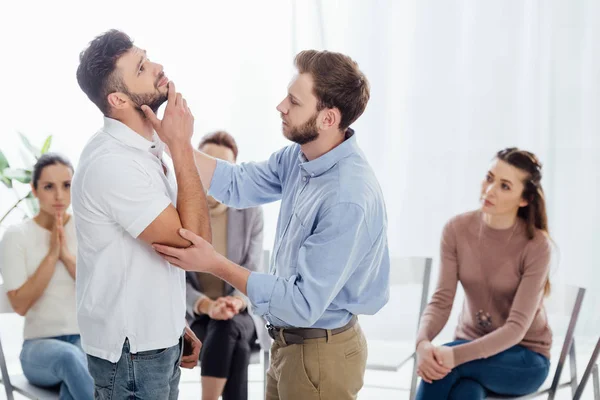 Mann tröstet einen anderen Mann, während Menschen während einer Gruppentherapie auf Stühlen sitzen — Stockfoto