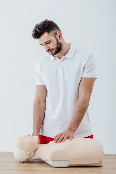 Hombre guapo mirando maniquí cpr durante el entrenamiento de primeros auxilios aislado en gris - foto de stock