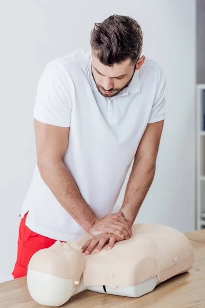 Красивый мужчина, использующий технику компрессии грудной клетки на манекене во время тренировок CPR — стоковое фото