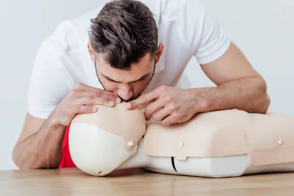 Uomo che utilizza la tecnica bocca a bocca sul manichino durante l'allenamento cpr isolato su grigio — Foto stock