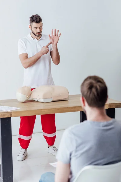 Enfoque selectivo del instructor guapo señalando con el dedo durante la clase de entrenamiento de primeros auxilios - foto de stock