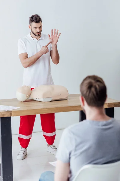 Selektiver Fokus eines gut aussehenden Ausbilders, der beim Erste-Hilfe-Kurs mit dem Finger zeigt — Stockfoto