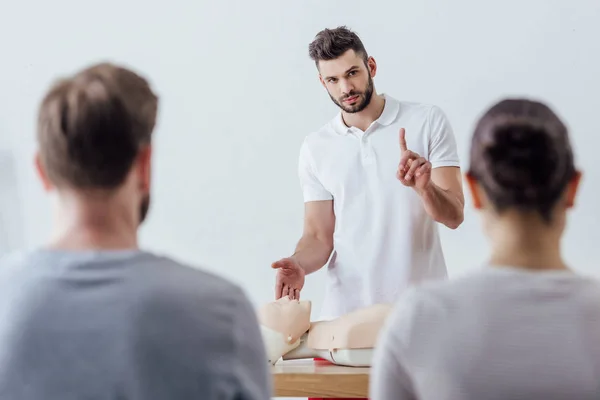 Instructor guapo con maniquí cpr apuntando con el dedo durante la clase de entrenamiento de primeros auxilios - foto de stock
