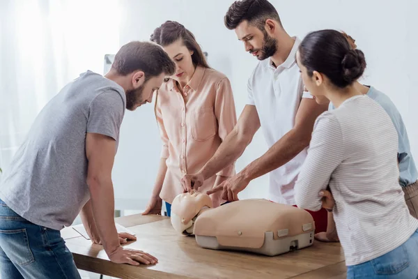 Groupe de personnes concentrées avec mannequin cpr pendant la classe de formation aux premiers soins — Photo de stock