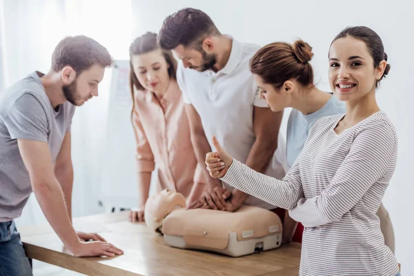 Woman showing thumb up while group of people performing cpr on dummy during first aid training — Stock Photo