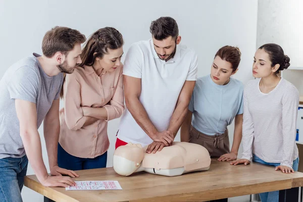 Group of people looking at man performing cpr on dummy during first aid training — Stock Photo