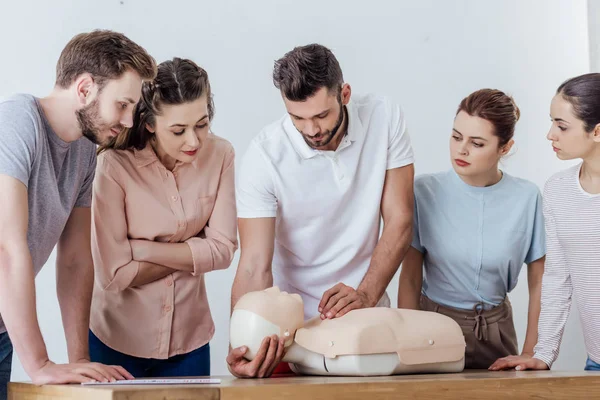 Groupe de personnes concentrées avec mannequin cpr pendant la classe de formation aux premiers soins — Photo de stock