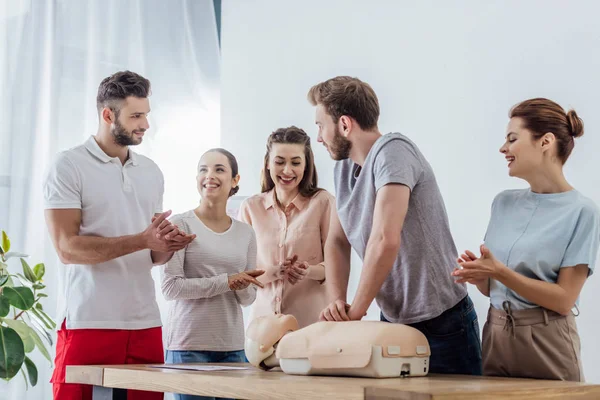 Grupo de personas aplaudiendo mientras el hombre realiza cpr en maniquí durante el entrenamiento de primeros auxilios - foto de stock