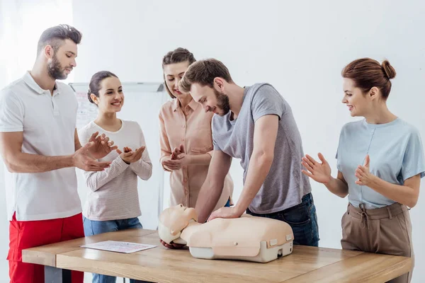 Група людей аплодує, коли чоловік виконує cpr на манері під час навчання першої допомоги — стокове фото