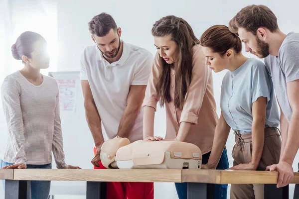 Groupe de personnes concentrées effectuant cpr sur mannequin pendant la formation de premiers soins — Photo de stock
