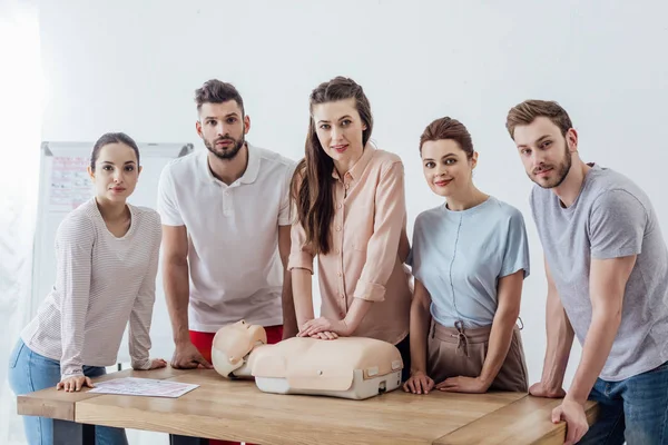 Gruppe von Menschen blickt während des CPR-Trainings mit Dummy in die Kamera — Stockfoto