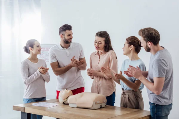 Group of smiling people with cpr dummy applauding during first aid training class — Stock Photo