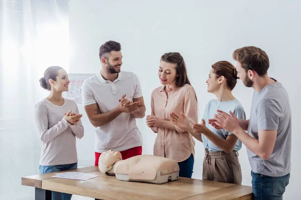 Grupo de pessoas sorrindo com aplausos boneco cpr durante a aula de treinamento de primeiros socorros — Fotografia de Stock