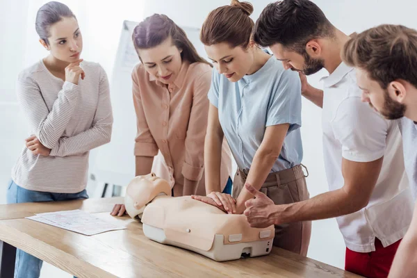 Grupo de pessoas focadas executando cpr no boneco durante o treinamento de primeiros socorros — Fotografia de Stock