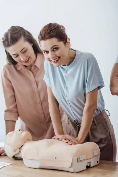 Lächelnde Frau, die Brustkompression auf einer Attrappe durchführt und während des CPR-Trainings in die Kamera schaut — Stockfoto