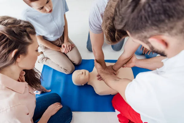 Hochwinkelaufnahme eines Instruktors, der während einer Erste-Hilfe-Ausbildung mit einer Gruppe von Personen cpr auf einer Attrappe durchführt — Stockfoto