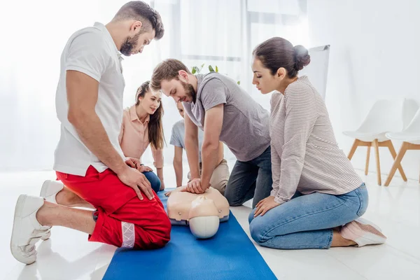 Grupo de personas mirando al hombre realizando cpr en maniquí durante el entrenamiento de primeros auxilios - foto de stock