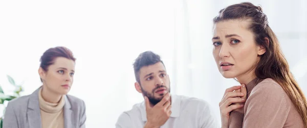 Foto panorámica de la mujer preocupada mirando a la cámara durante la sesión de terapia de grupo - foto de stock