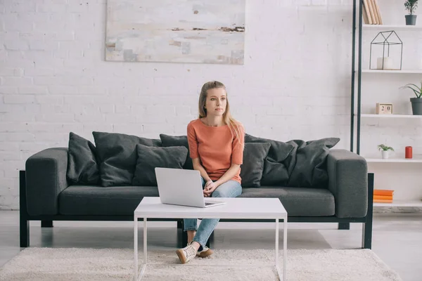 Bela loira freelancer sentado no sofá perto de laptop em casa — Fotografia de Stock