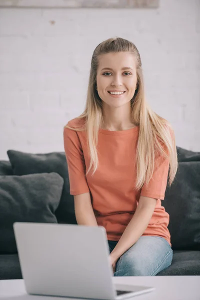 Счастливая блондинка-фрилансер сидит дома на диване рядом с ноутбуком — стоковое фото