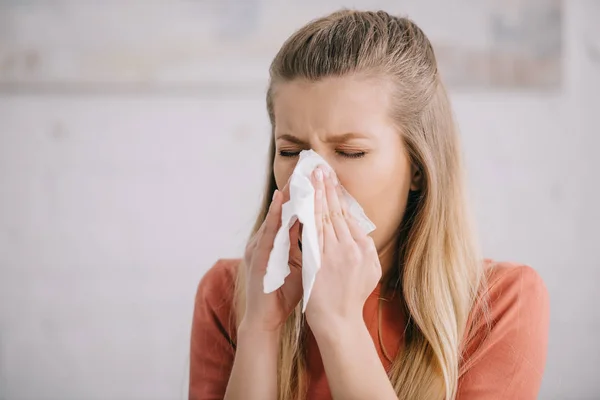 Blonde woman sneezing while holding tissue near nose — Stock Photo