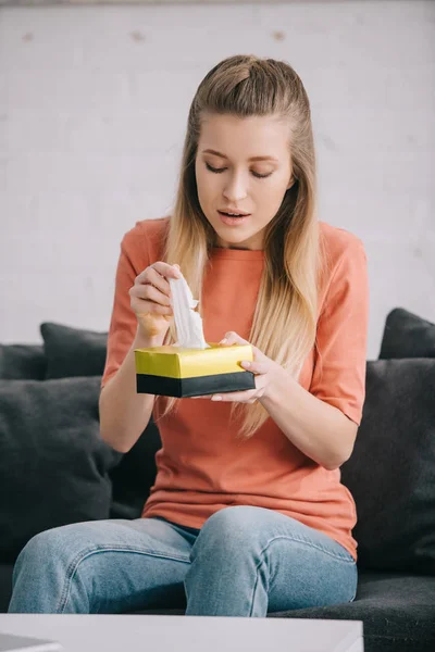 Blonde woman holding tissue box while sitting on sofa at home — Stock Photo