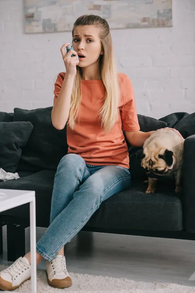 Belle femme blonde allergique au chien en utilisant un inhalateur tout en étant assis près du chien mignon à la maison — Photo de stock