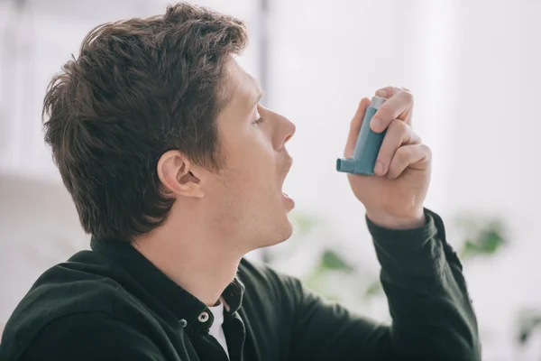 Vue latérale du bel homme utilisant un inhalateur à la maison — Photo de stock