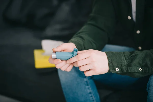 Cropped view of man holding inhaler while sitting on sofa — Stock Photo