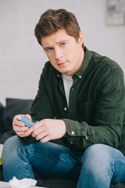 Handsome man holding inhaler while sitting on sofa — Stock Photo