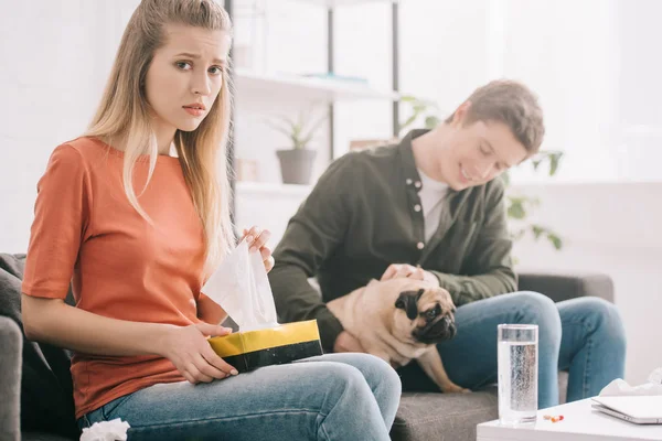 Selektiver Fokus einer aufgebrachten blonden Frau, die allergisch auf Hundehalter mit Gewebebox in der Nähe eines Mannes mit Mops reagiert — Stockfoto