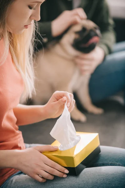 Selective focus of sad blonde woman holding tissue box near man with dog — Stock Photo