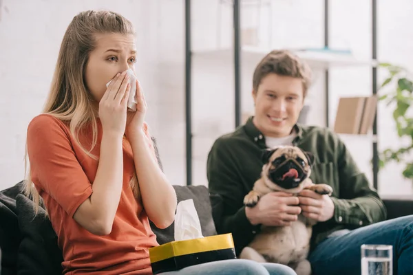 Selective focus of woman allergic to dog sneezing near cheerful man with pug — Stock Photo