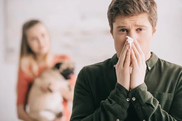 Селективное внимание мужчины аллергия на чихание собаки в тканях и взгляд на камеру рядом с женщиной с мопсом — стоковое фото